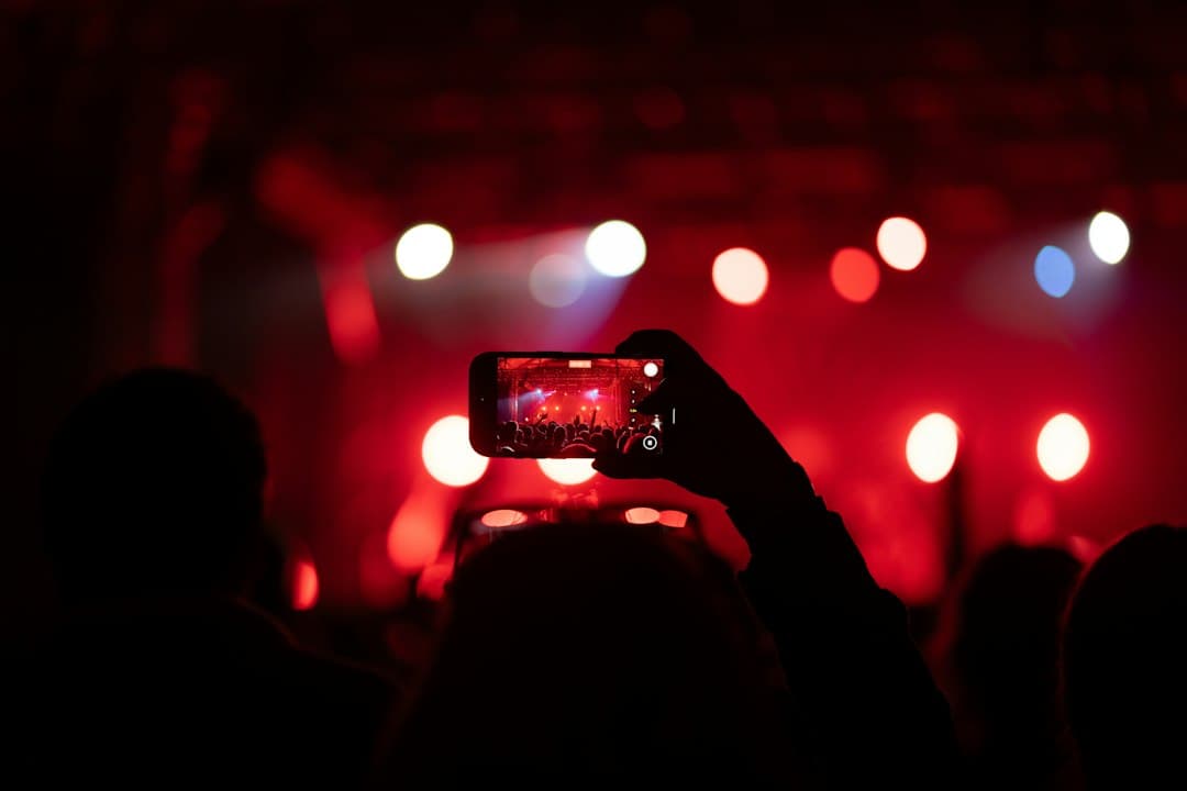 Ein Handy wird bei einem Konzert hochgehalten, auf dem Display Bühne und Lichter