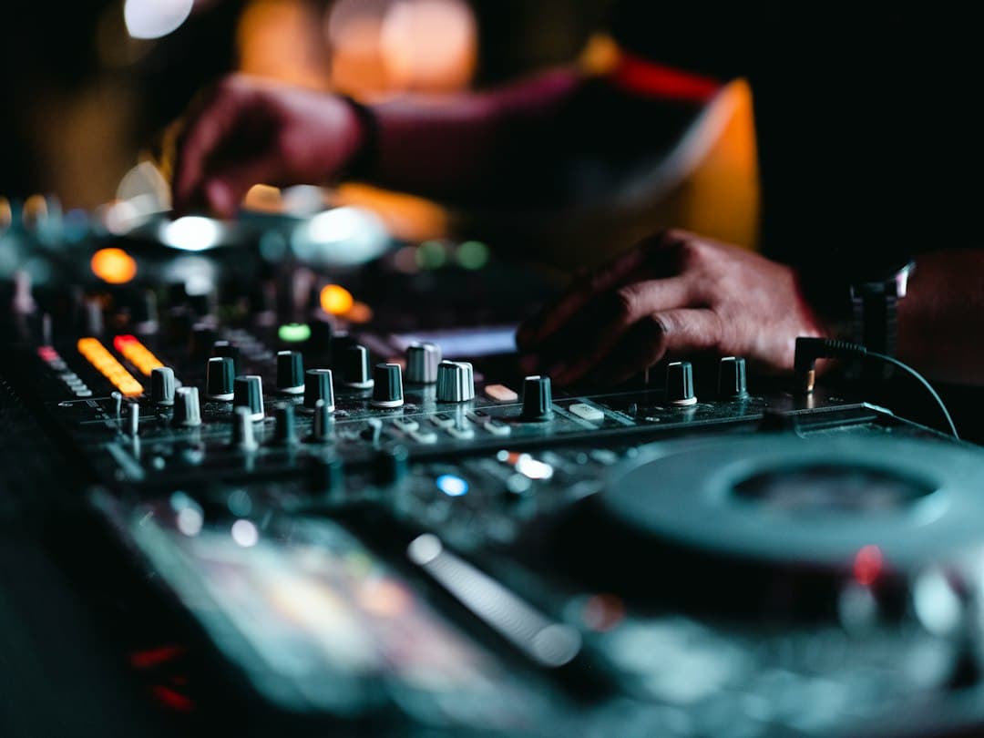 Ein DJ am Pult in einem dunklen Club, die Hände am Mixer