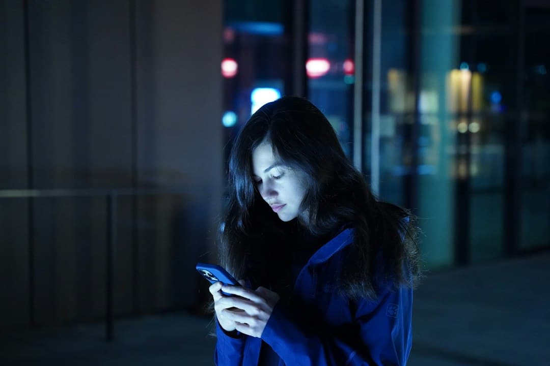 Eine Frau in blauer Jacke schaut am Abend draußen konzentriert auf ihr Handy