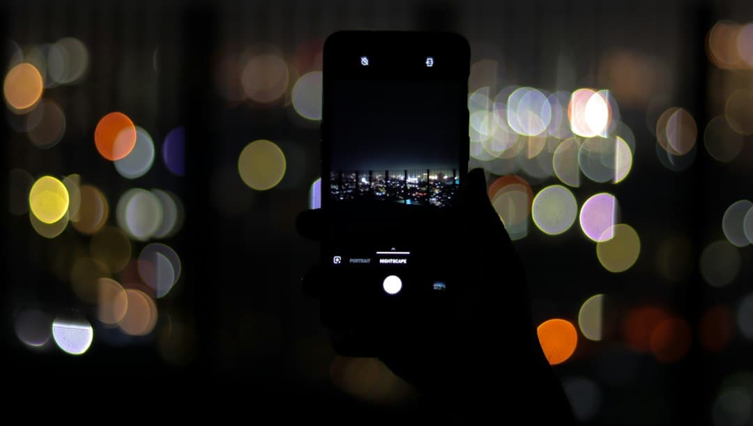 Ein Smartphone wird nachts vor unscharfen Lichtern der Stadt hochgehalten